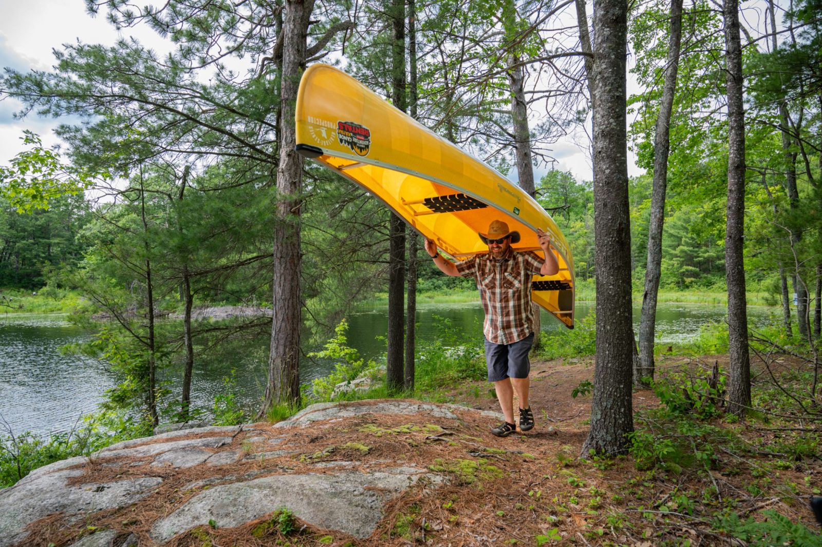 Camper carrying a lightweight Kevlar canoe on a portage trail during a backcountry canoe trip in Kawartha Highlands Provincial Park.